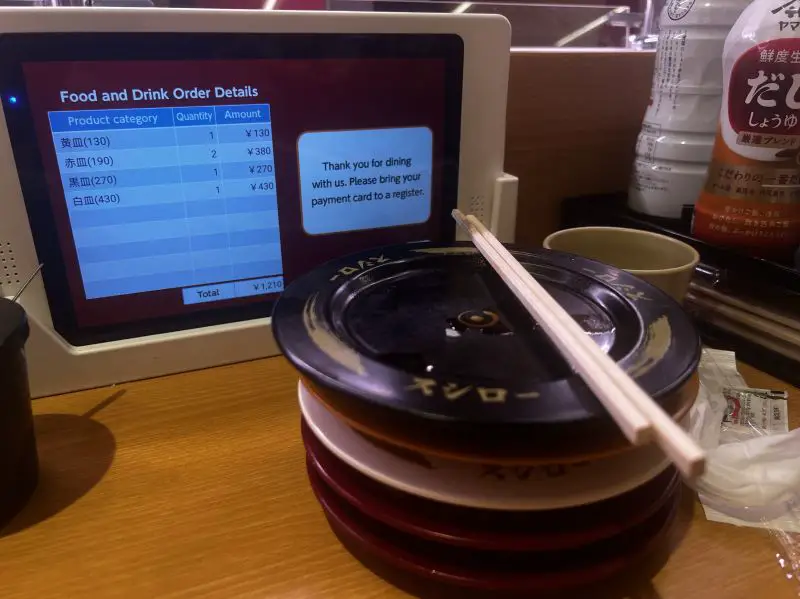 A stack of plates in front of a tablet showing the final cost of the sushi eaten at Sushiro