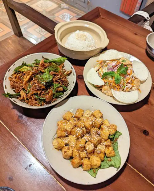 An top down view of vegan food - fried tofu with sesame seeds, crispy mushrooms with lemongrass, and vegetarian Vietnamese salad with rice crackers - at Thong Dong Vegan 2 in Sapa, Vietnam