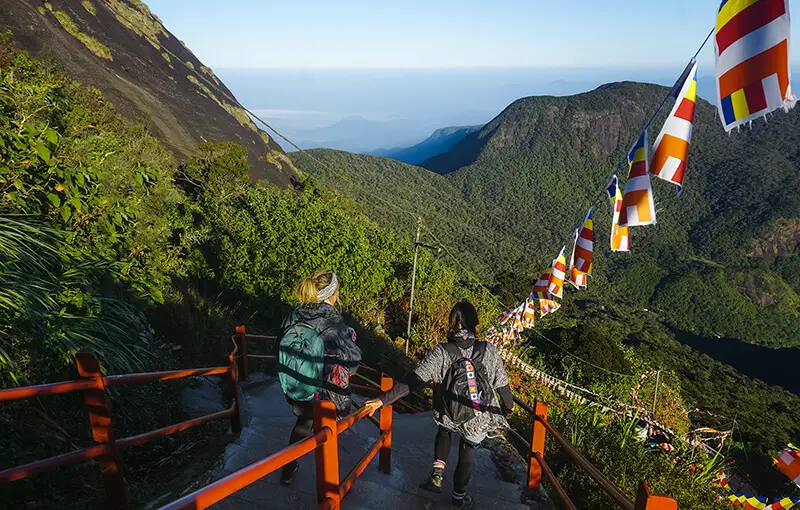 Two hikers wearing backpacks descending a staircase of the mountainous Adam's Peak in Sri Lanka