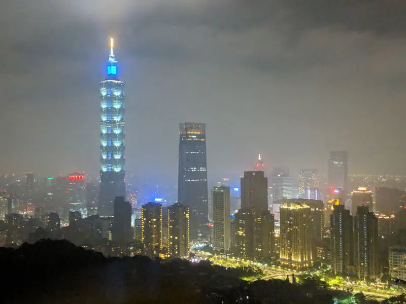 View of Taipei's skyscrapers and Taipei 101 Building illuminating a blue and aqua color at night time from Elephant Mountain Trail