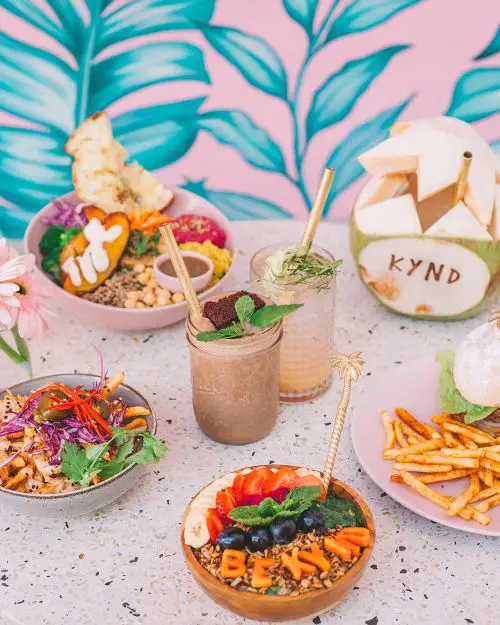 A table of brunch foods such as granola smoothie bowl, fries, rice bowl, burger and fries, fresh coconut drink , and two smoothies at KYND Community in Seminyak, Bali