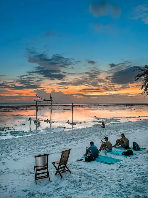 Three people sitting on one of Gili Trawangan's white sandy beach at sunset