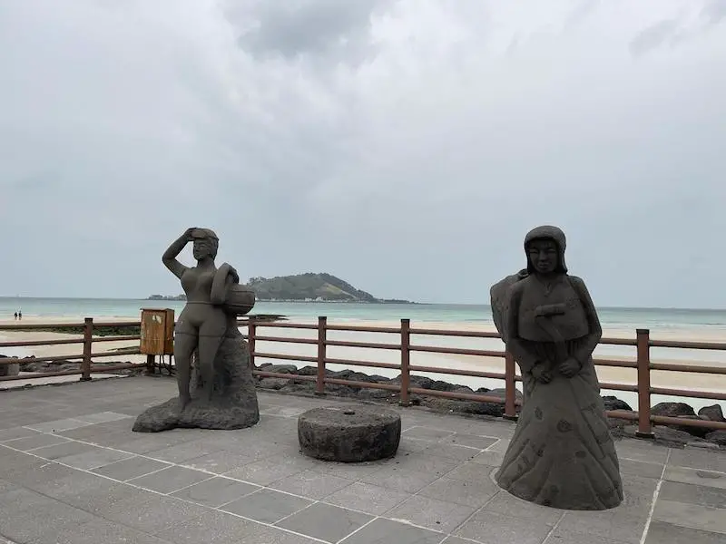 Two statues of Haenyeo women divers next to a beach on Jeju Island, South Korea