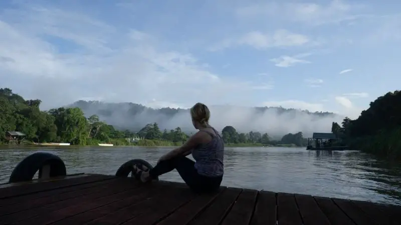 A woman sits on the wooden deck and overlooks the Kinabatangan River in Malaysia