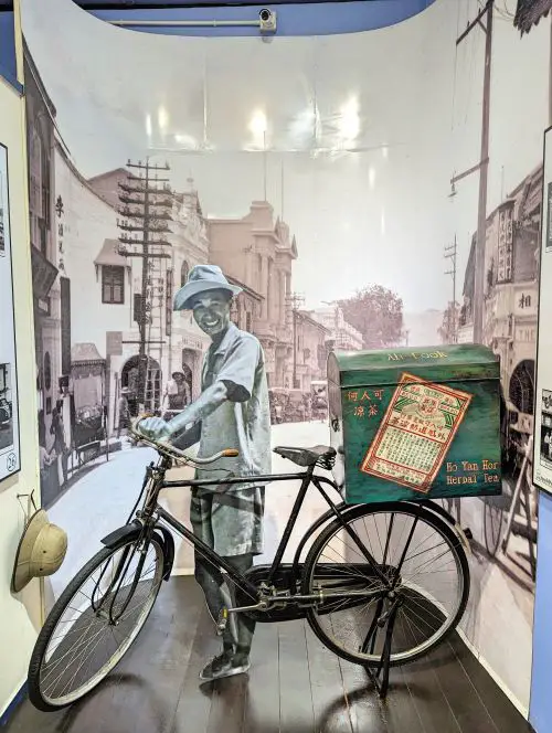 A cardboard photo of Dr. Ho Kai Cheong next to a bicycle to make herbal tea deliveries at Ho Yan Hor Museum