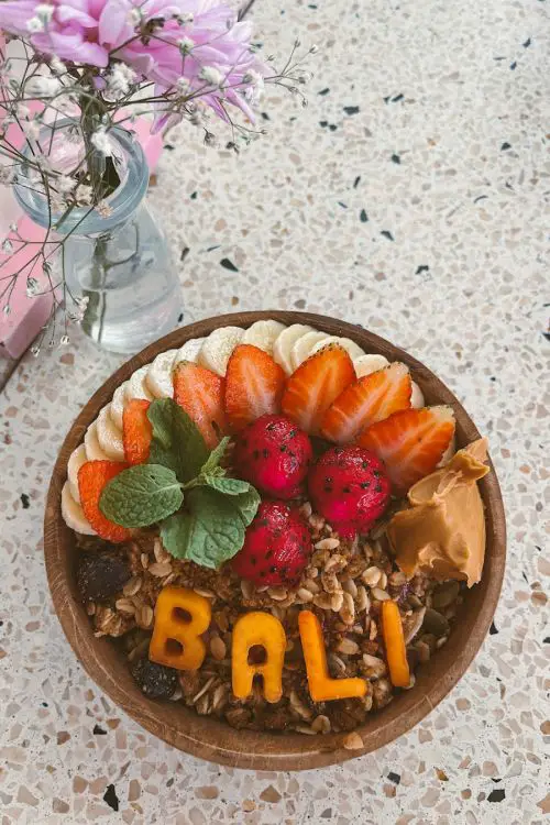 A smoothie bowl with peanut butter, dragon fruit, sliced strawberries and bananas, oatmeal, and the word, BALI, made out of orange colored fruit