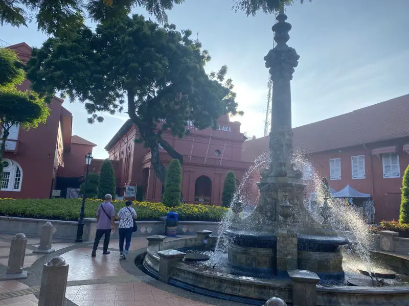 A man and woman walk around the Queen Victoria water fountain at Dutch Square in Melaka, Malaysia