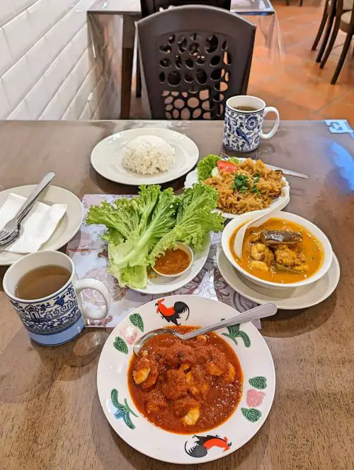 A wooden table with three dishes of Nyonya food such as fish curry, sambal shrimp, and stir fried yam beans with cuttlefish at Bibik's Kitchen in Penang, Malaysia