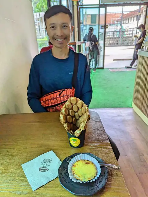 Justin Huynh, Life Of Doing, smiles with the durian bubble waffle and the cheese durian tart at Durian Baby and Friends in Penang