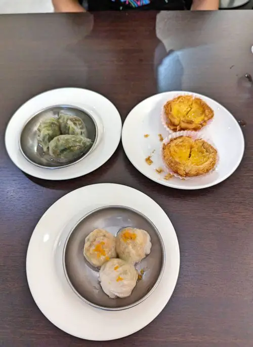 A table with three plates of dim sum of shrimp dumplings, egg tarts, and vegetarian dumplings at Food Dynasty in Penang