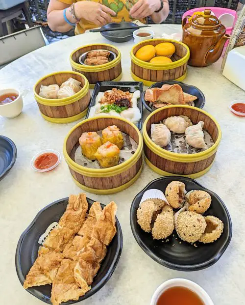 A marble table with small dishes of dim sum such as sesame balls, crispy shrimp rolls, steamed pork dumplings, steamed shrimp dumplings, steamed shrimp rolls, steamed buns, and more at Fu Er Dai in Penang