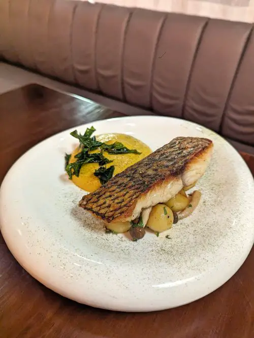 A white curved plate with pan fried fish with potato and mushroom and a side of tumeric cream at Hygge Dining in Penang