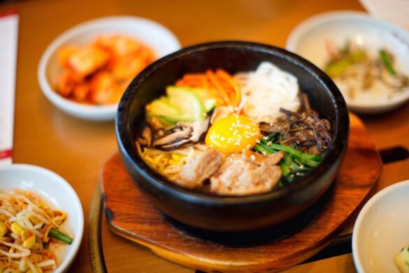 A table with a stone pot of bibimbap, rice with vegetables and raw egg, and small dishes of bean sprouts and kimchee