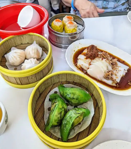 A white table with bamboo steamers of steamed vegetable dumplings and steamed shrimp dumplings and a plate of steamed shrimp rolls at Tai Tong Restaurant