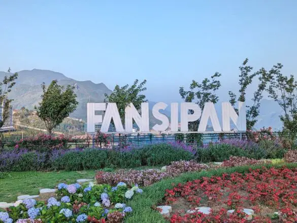 A garden with hydrangeas, purple flowers, and red flowers with a large Fansipan sign
