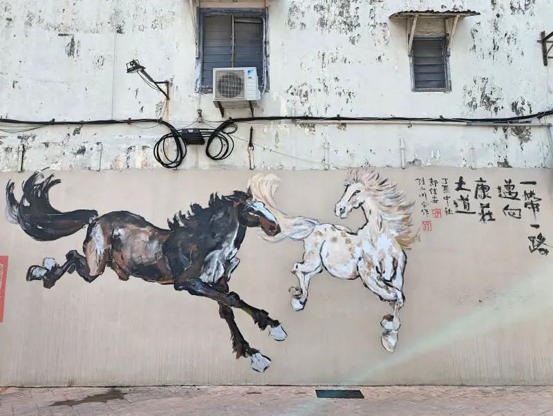 The Horses mural in Melaka of a white and cream colored horse and a black, brown, and white horse galloping