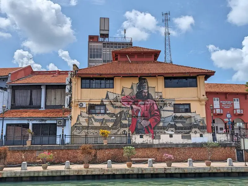 One of the wall arts on along the Melaka River of a soldier wearing a red jacket and in front of a palace