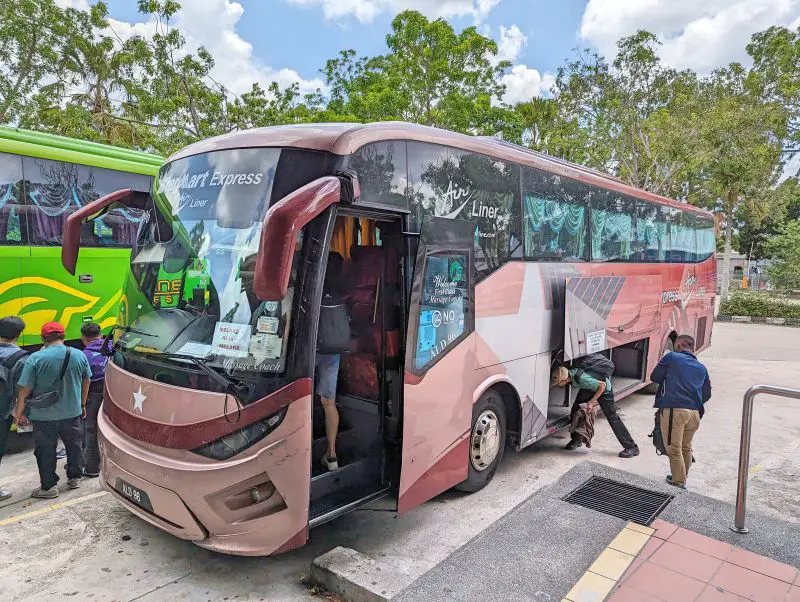 A pink and red Starmart Bus parked at Melaka Sentral Station and waiting for people to board and load their luggage in the undercarriage