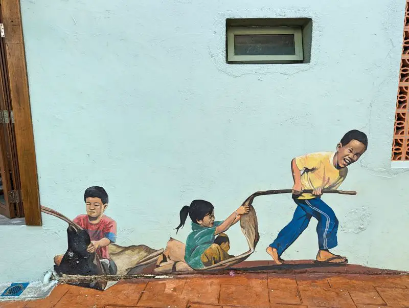 A street art of three kids playing with dried leaves in Melaka's The Well street
