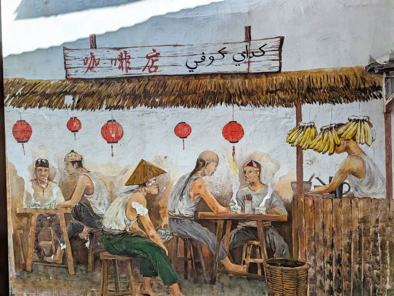 A street art in Melaka's The Well of five men sitting on stools and drinking hot coffee