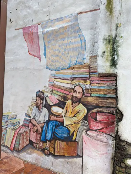 A street art in Melaka's The Well of two men sitting on a box and waiting for customers to sell fabrics