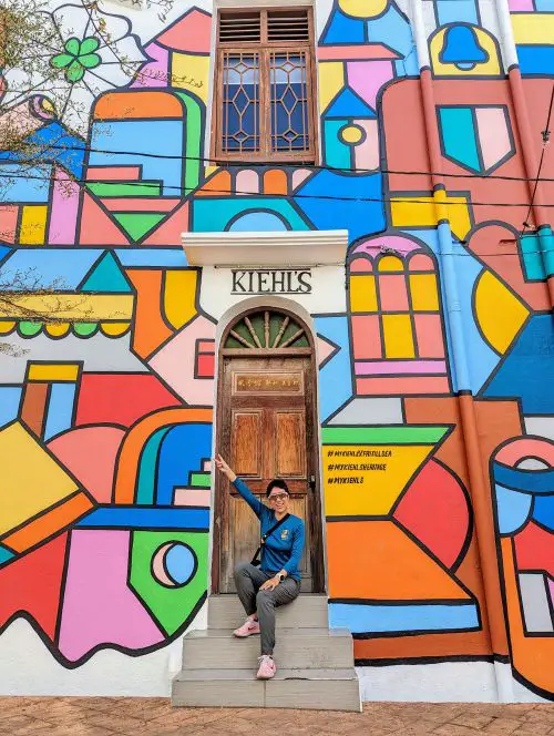 Jackie Szeto, Life Of Doing, sits on the steps in front of the colorful My Kiehl's Heritage doorway and wall art in Melaka, Malaysia