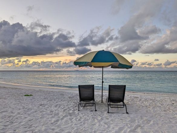 Two lawn chairs and an umbrella on the white sandy beach of Fulidhoo Island, Maldives at sunrise