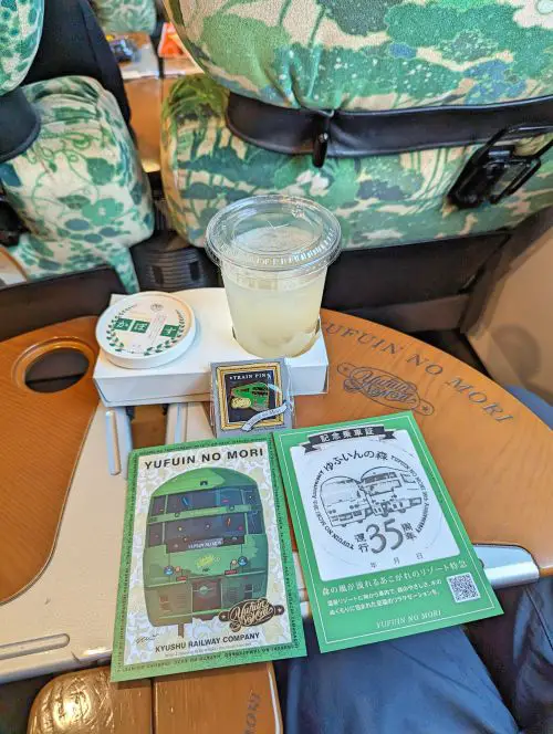 A yuzu honey drink, ice cream, train pin, and two Yufuin no Mori postcards with stamps on the seat table