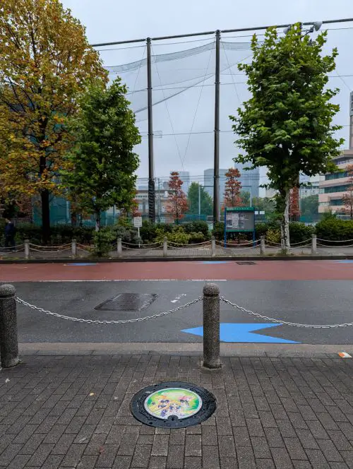 A street view of the the green manhole cover of the Sailor Moon's Sailor Guardians across from the Shiba Water Supply Station Park