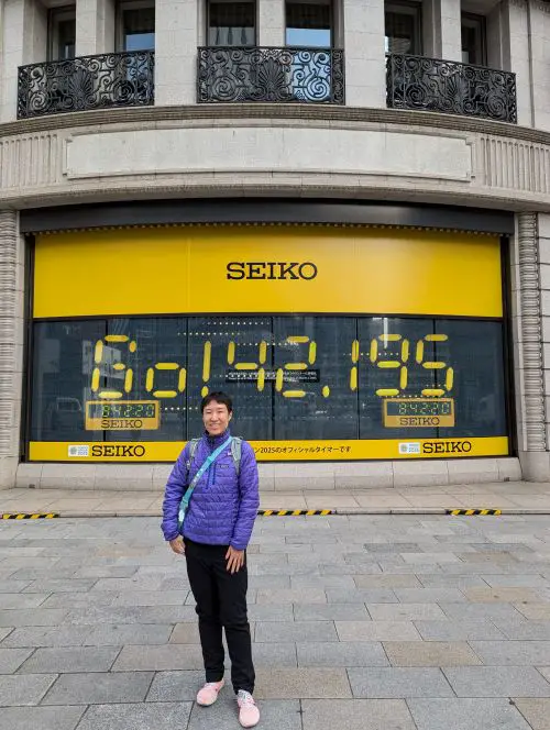Jackie Szeto, Life Of Doing, stands in front of the Seiko Building with a list of all the runners in the Ginza area