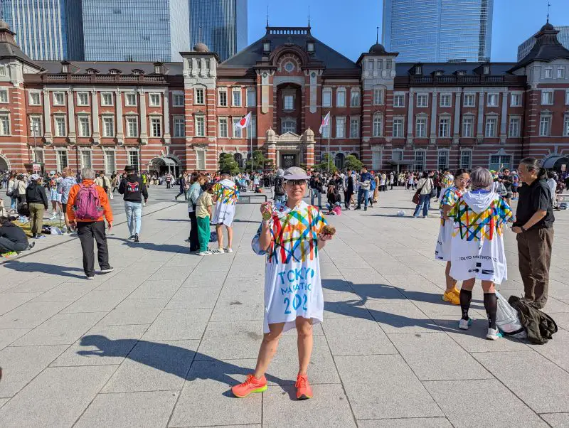 Jackie Szeto, Life Of Doing, poses with Tokyo Marathon medal and wears the finisher's poncho in front of Tokyo Station