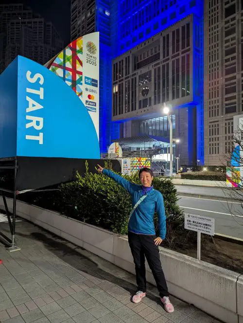 Jackie Szeto, Life Of Doing, stands next to the Tokyo Marathon 2025 Start Line at night