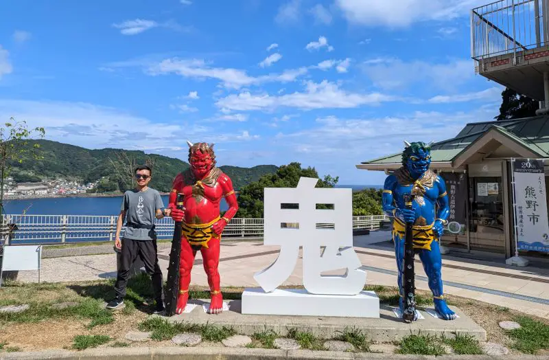 Justin Huynh, Life Of Doing, stands next to the red demon at the Onigajo entrance. Entrance also has a blue demon and the white Japanese Kanji character of demon.