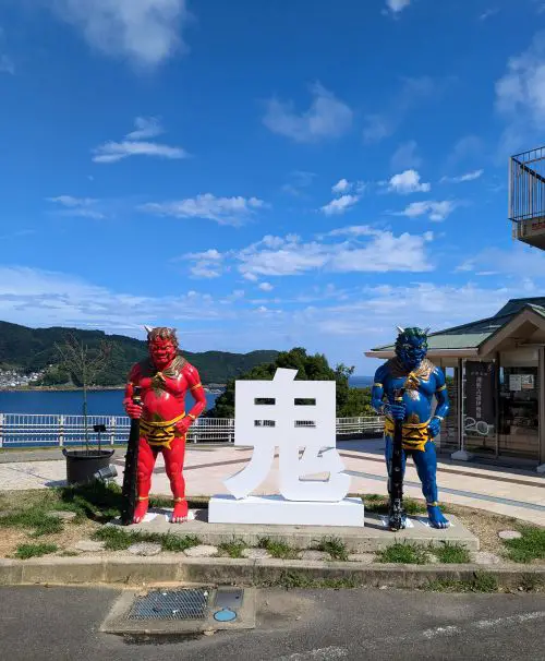 A red and blue demon statues and a white kanji character of demon in Japanese, located at the Onigajo Cliffside in Kumano, Japan.