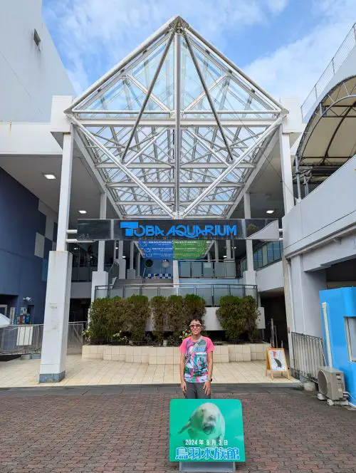 Jackie Szeto, Life Of Doing, stands at the entrance of Toba Aquarium with a sign of Serena the dugong