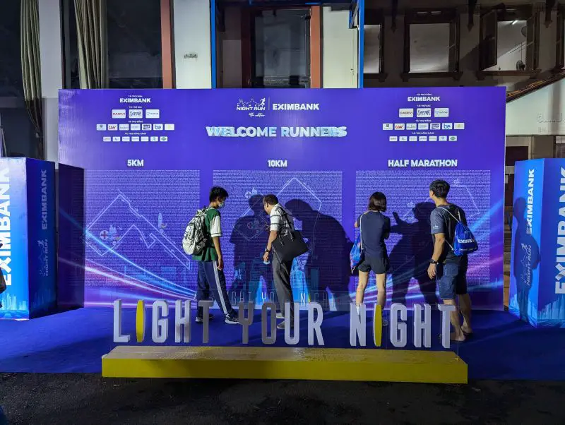 Four people at the HCMC Night Run board looking for their names on the 5 km, 10 km, and half marathon course map