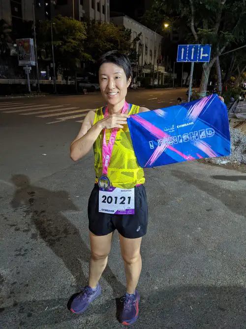 Jackie Szeto, Life Of Doing, wears her HCMC Night Run Half Marathon finisher's medal and holds the I FINISHED towel