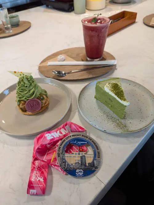 The Ho Chi Minh City Night Run finisher medal next to a plate of matcha millecrepe, matcha Saint honore dessert, and a cherry juice at Miyama Cafe