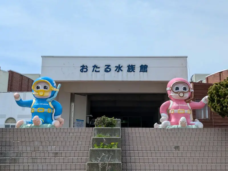 Two octopus statues wearing a pink and blue scuba diving gear in front of the Otaru Aquarium entrance