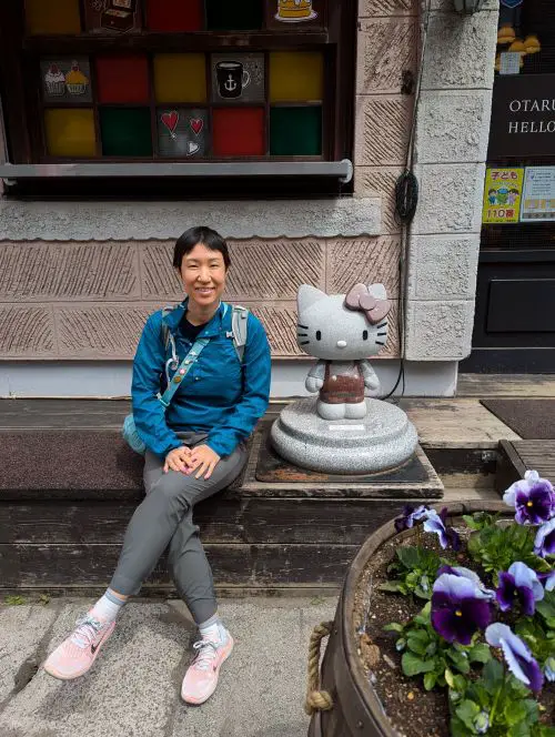 Jackie Szeto, Life Of Doing, sits next to the Hello Kitty statue in front of Otaru's Hello Kitty cafe
