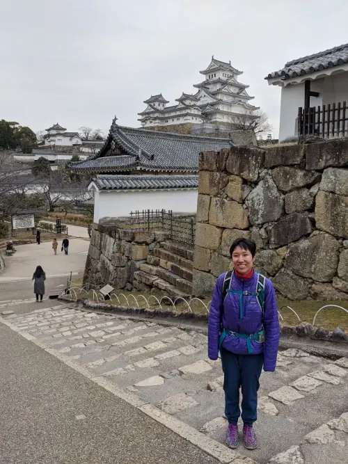 Jackie Szeto, writer of Life Of Doing, stands next to a stoned wall and has a view of Himeji Castle in the background