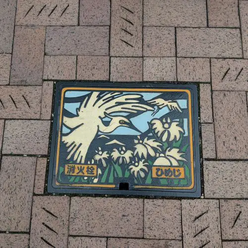 A manhole cover in Himeji of a white heron with white flowers