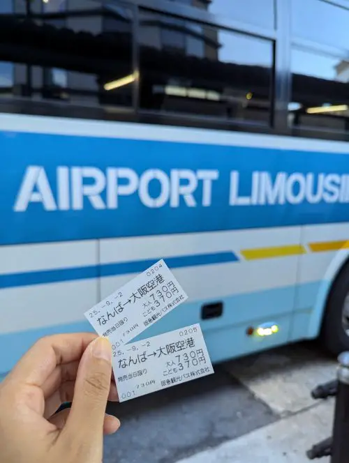 A hand holding two bus tickets from Namba to Osaka Itami Airport