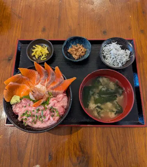 A top down view of a mashed tuna, salmon, and shrimp rice bowl with a side of miso soup, whitebait fish, and pickles at Oma Tuna, Shimizu Fish Market