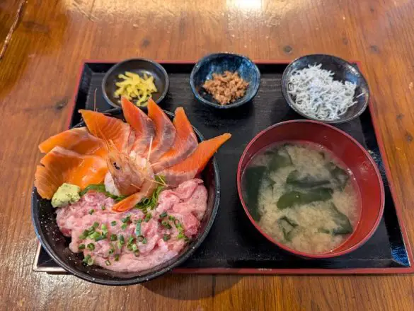 A seafood rice bowl with chopped tuna and green onions, shrimp, and salmon and side items of miso soup, whitebait fish, and pickles at Oma Tuna, Shimizu Fish Market