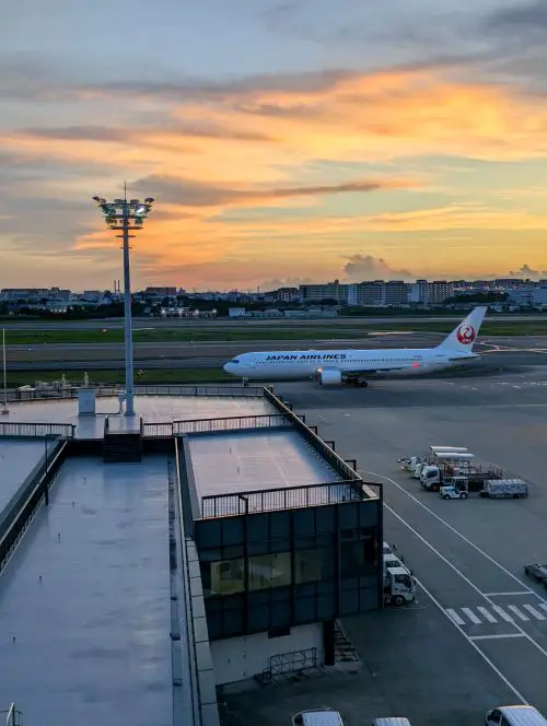 A Japan Airlines airplane is on the Osaka Itami Airport tarmac at sunset
