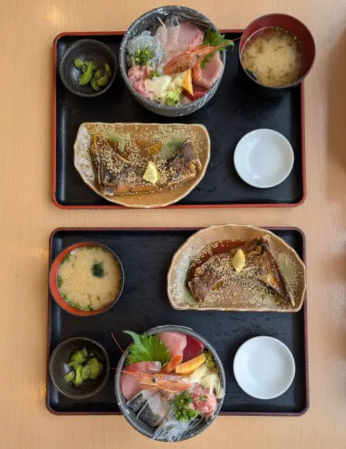 A top down view of two black trays with seafood rice bowls, fish jaw, miso soup, and pickles at Totosuke restaurant, Shimizu Fish Market