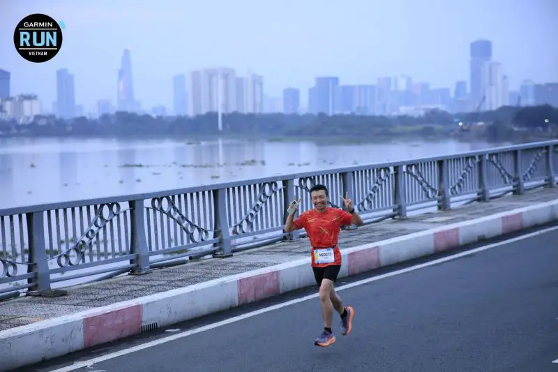 Justin Huynh, Life Of Doing, smiles and holds peace signs for the camera on the bridge during the Garmin Run Vietnam half marathon