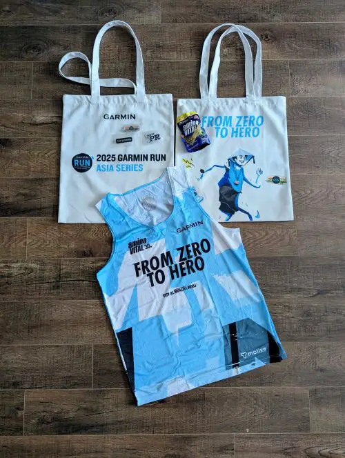 A top down photo of the Garmin Run Vietnam swag such as the tote bag, singlet for half marathon participants, acrylic badges, and an Amino Vital energy gel