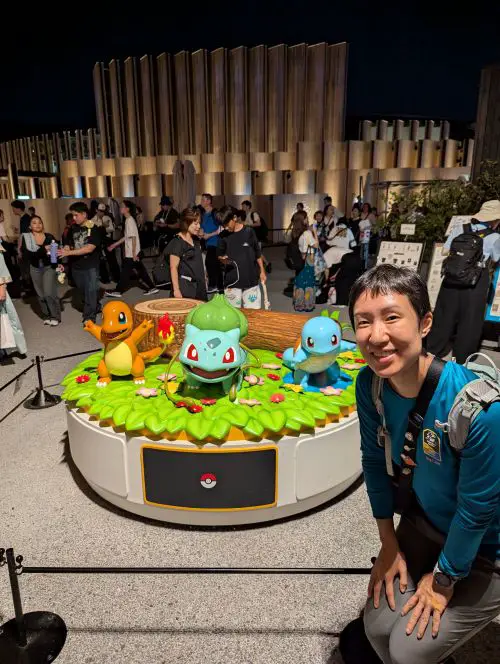 Jackie Szeto, Life Of Doing, poses next to the three Pokémon statues, Charmander, Squirtle, and Bulbasaur